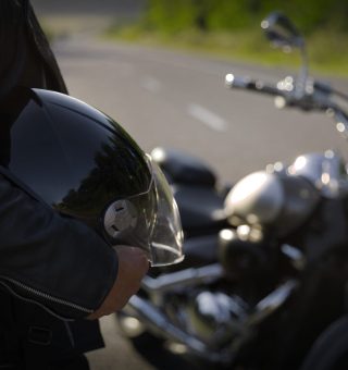 Homem parado com capacete na mão ao lado de moto