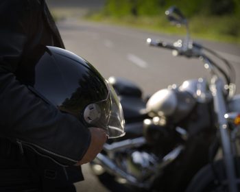 Homem parado com capacete na mão ao lado de moto